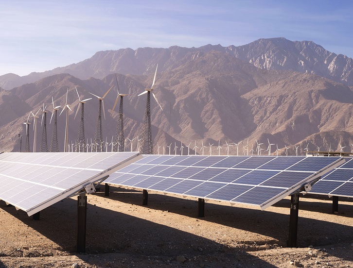 A large solar power farm with wind turbines in the background